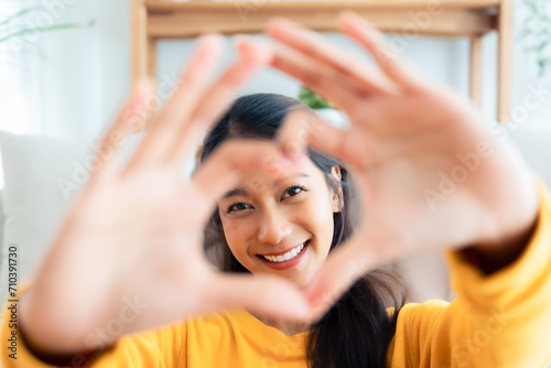 Bild auf Leinwand Front view of cute young Asian woman smiling and looking at camera with hands showing heart shape