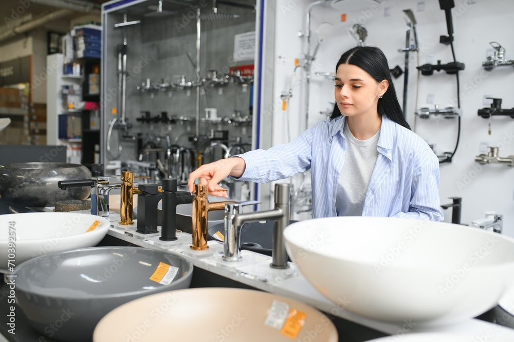 Woman inspects and chooses new kitchen or bath tap faucet at a hardware store Woman inspects and chooses new kitchen or bath tap faucet at a hardware store