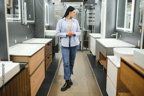 Young woman choosing new bathroom furniture at the plumbing shop with lots of sanitary goods
