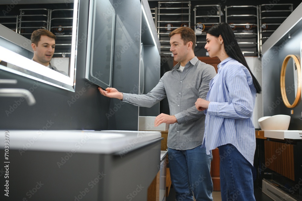 Fototapeta premium Young couple choosing new bathroom furniture at the plumbing shop with lots of sanitary goods
