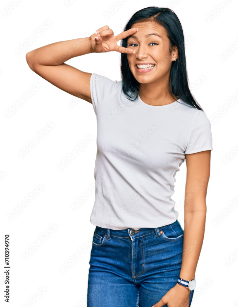 Beautiful hispanic woman wearing casual white tshirt doing peace symbol with fingers over face, smiling cheerful showing victory Beautiful hispanic woman wearing casual white tshirt doing peace symbol with fingers over face, smiling cheerful showing victory