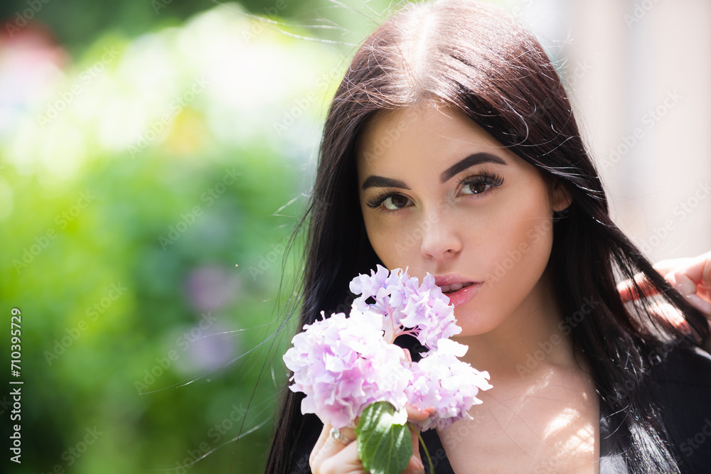 Fototapeta premium Young woman near blossom park. Spring girl. Woman on spring blooming tree. Beautiful young woman in summer style outfit with flowers outdoor. Spring sunshine park. Beauty woman enjoying smell in a