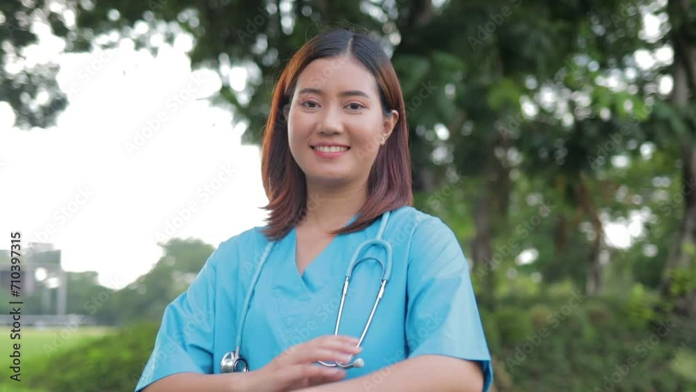 Portrait of a beautiful smiling Asian female doctor wearing a blue surgical gown standing in an outdoor garden. medical concept Portrait of a beautiful smiling Asian female doctor wearing a blue surgical gown standing in an outdoor garden. medical concept