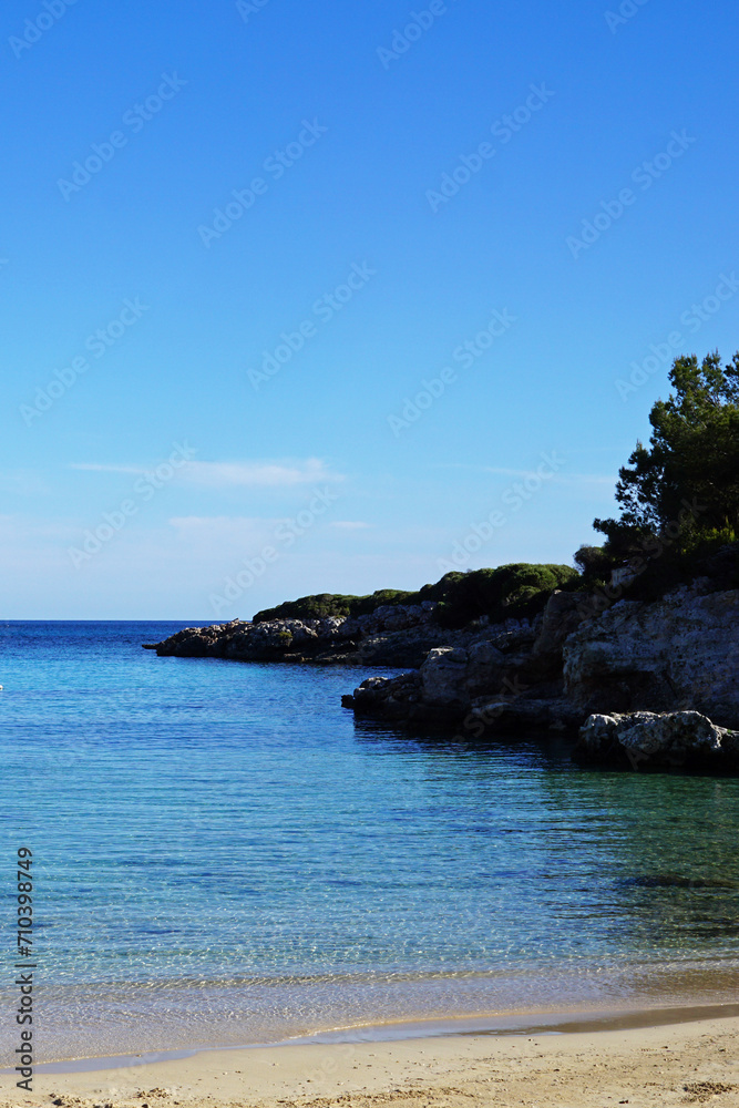 Natural landscape of Playa de Cavalleria (Mercadal) in Minorca beach with clear blue sky and rocky seashore- Menorca, Spain