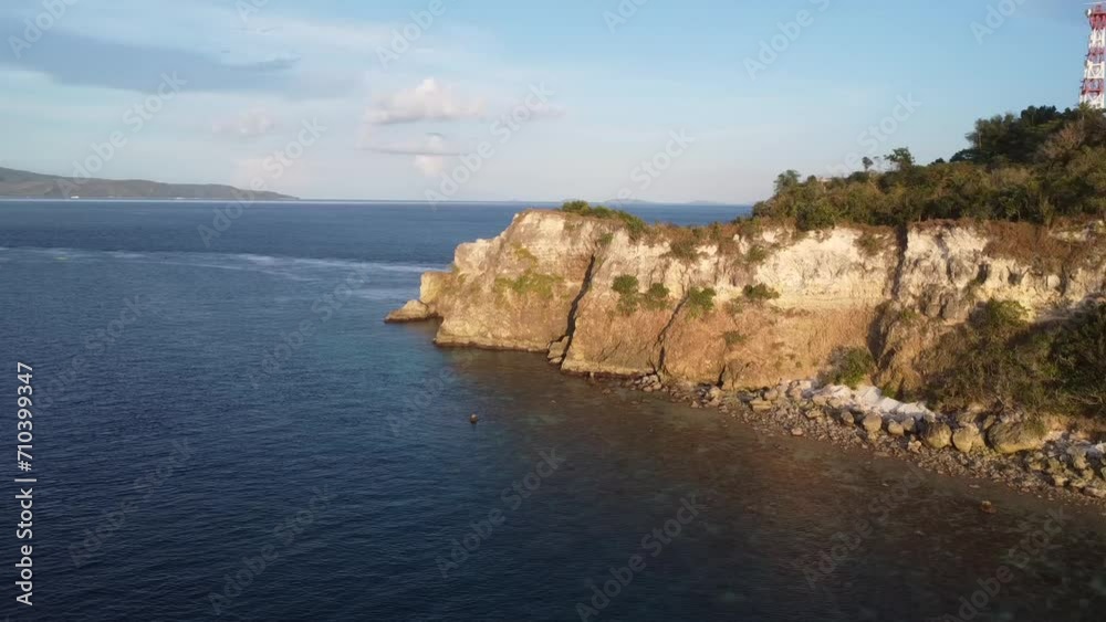 Aerial view of the rocky coast of a tropical island at sunset. Flight over a calm sea along a rocky cliff of a tropical island at sunset. Aerial view of the rocky coast of a tropical island at sunset. Flight over a calm sea along a rocky cliff of a tropical island at sunset.