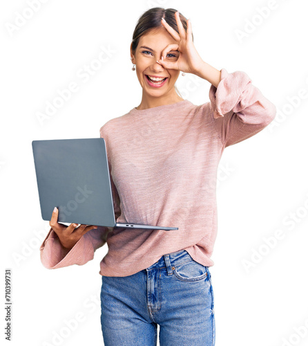 Beautiful caucasian woman with blonde hair working using computer laptop smiling happy doing ok sign with hand on eye looking through fingers © Krakenimages.com