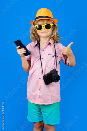 Child tourist. Photo of cute child boy using mobile phone isolated over blue studio background. Portrait of kid tourist traveller. Kids travel concept. Child ready for vacation.