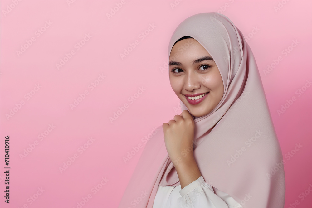 Beautiful young Muslim woman wearing hijab, smiling and looking at camera on pale pink background Beautiful young Muslim woman wearing hijab, smiling and looking at camera on pale pink background
