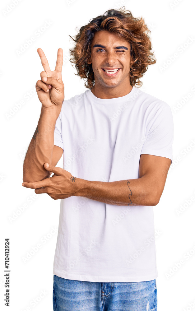 Young hispanic man wearing casual white tshirt smiling with happy face winking at the camera doing victory sign with fingers. number two. Young hispanic man wearing casual white tshirt smiling with happy face winking at the camera doing victory sign with fingers. number two.