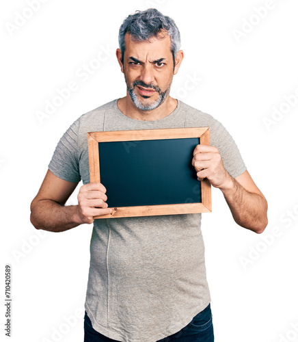 Middle age hispanic man with grey hair holding blackboard clueless and confused expression. doubt concept.