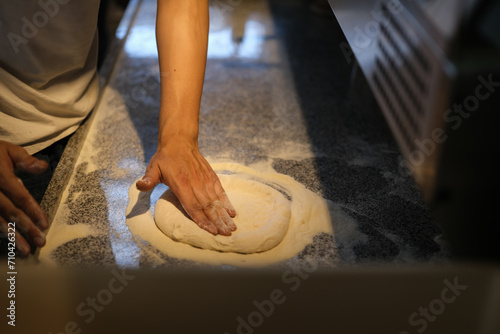 Chef kneading pizza dough with flour on kitchen table. Bakery or pizza baking concept