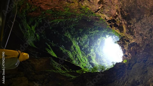 Tourist explores Algar do Carvao volcanic tube in Terceira, Azores. Vertical photo