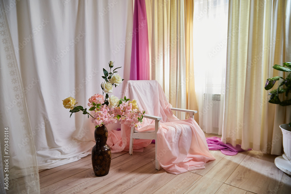 Delicate bright pink interior of the room with armchair, a vase with roses, draped curtains and a window. Location and background in the photo studio Delicate bright pink interior of the room with armchair, a vase with roses, draped curtains and a window. Location and background in the photo studio