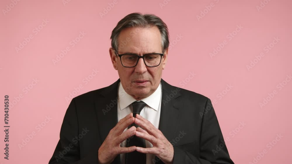 A contemplative businessman in formal attire makes calculated hand gestures for strategic planning on a pink backdrop. Camera 8K RAW. A contemplative businessman in formal attire makes calculated hand gestures for strategic planning on a pink backdrop. Camera 8K RAW.