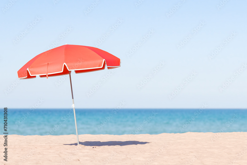 single red beach umbrella standing on a sandy beach with a clear blue sky and calm ocean in the background, peaceful beach day concept.