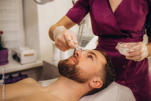 Cosmetologist applying mask on man's face in spa salon, top view