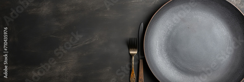 An empty black plate with cutlery on a dark concrete back.
