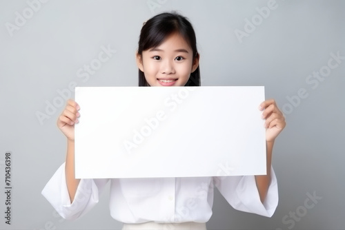 Happy asian scholl girl holding blank white banner sign, isolated studio portrait.