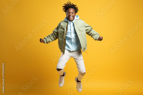 Portrait of jumping African-American teenage boy on color background.