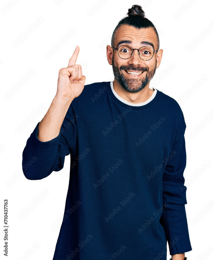 Hispanic man with ponytail wearing casual sweater and glasses pointing finger up with successful idea. exited and happy. number one. Hispanic man with ponytail wearing casual sweater and glasses pointing finger up with successful idea. exited and happy. number one.