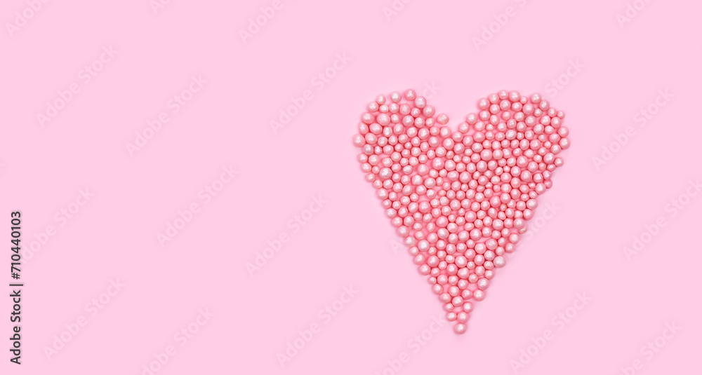 Heart shape made of small pink balls on pink background. Creative composition for Valentine's Day. Top view. Copy space.