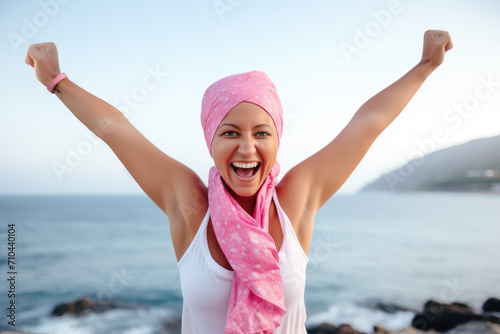 Joyful female cancer survivor raising arms in victory by the seaside, embodying hope and success. photo
