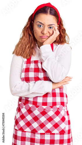 Young latin woman wearing apron thinking looking tired and bored with depression problems with crossed arms.