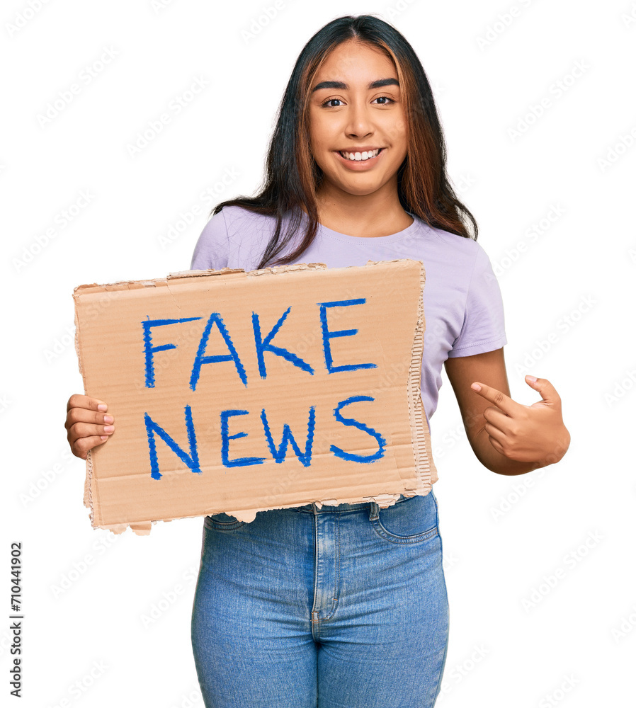 Young latin woman holding fake news banner smiling happy pointing with hand and finger Young latin woman holding fake news banner smiling happy pointing with hand and finger