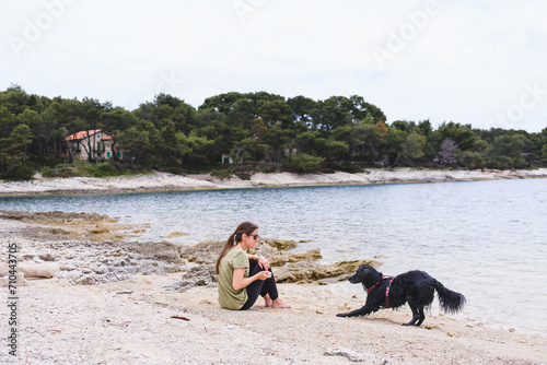 Young woman sitting on the beach and playing with her active dog. Healthy family pet enjoying time outside with owner.