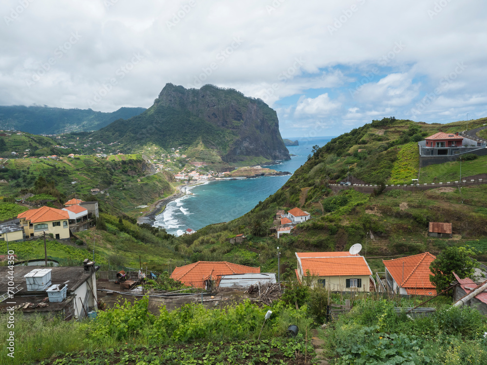 Obraz premium Aerial view of Porto da Cruz town with green cliff of Penha D'Aguia mountain and beautiful coast. Landscape scenery at the north of Madeira island, Portugal