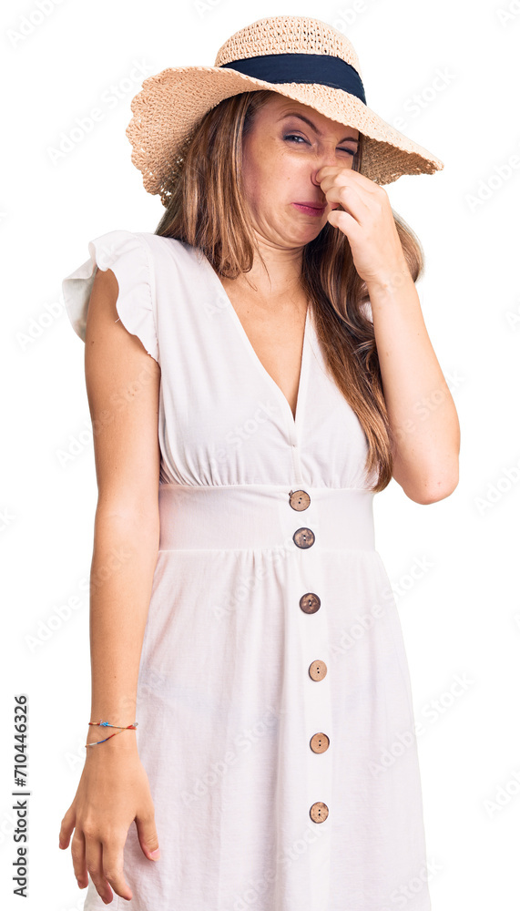 Young beautiful blonde woman wearing summer dress and hat smelling something stinky and disgusting, intolerable smell, holding breath with fingers on nose. bad smell Young beautiful blonde woman wearing summer dress and hat smelling something stinky and disgusting, intolerable smell, holding breath with fingers on nose. bad smell
