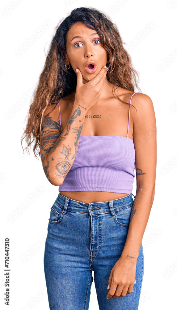 Young hispanic woman with tattoo wearing casual clothes looking fascinated with disbelief, surprise and amazed expression with hands on chin Young hispanic woman with tattoo wearing casual clothes looking fascinated with disbelief, surprise and amazed expression with hands on chin