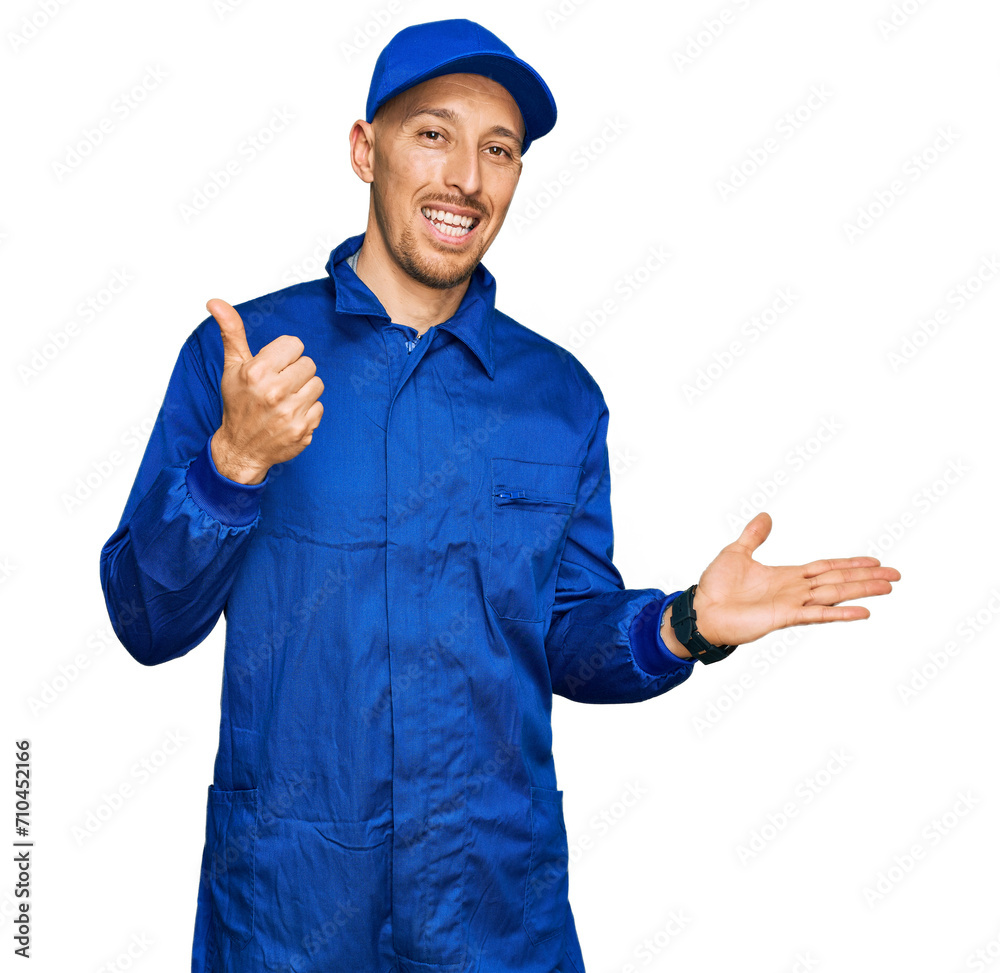 Bald man with beard wearing builder jumpsuit uniform showing palm hand and doing ok gesture with thumbs up, smiling happy and cheerful Bald man with beard wearing builder jumpsuit uniform showing palm hand and doing ok gesture with thumbs up, smiling happy and cheerful