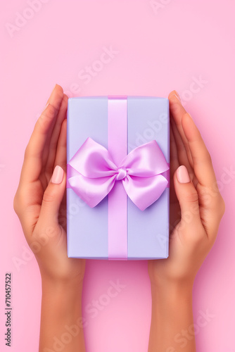 A woman's hands are holding a purple gift box with a bow. © Nell