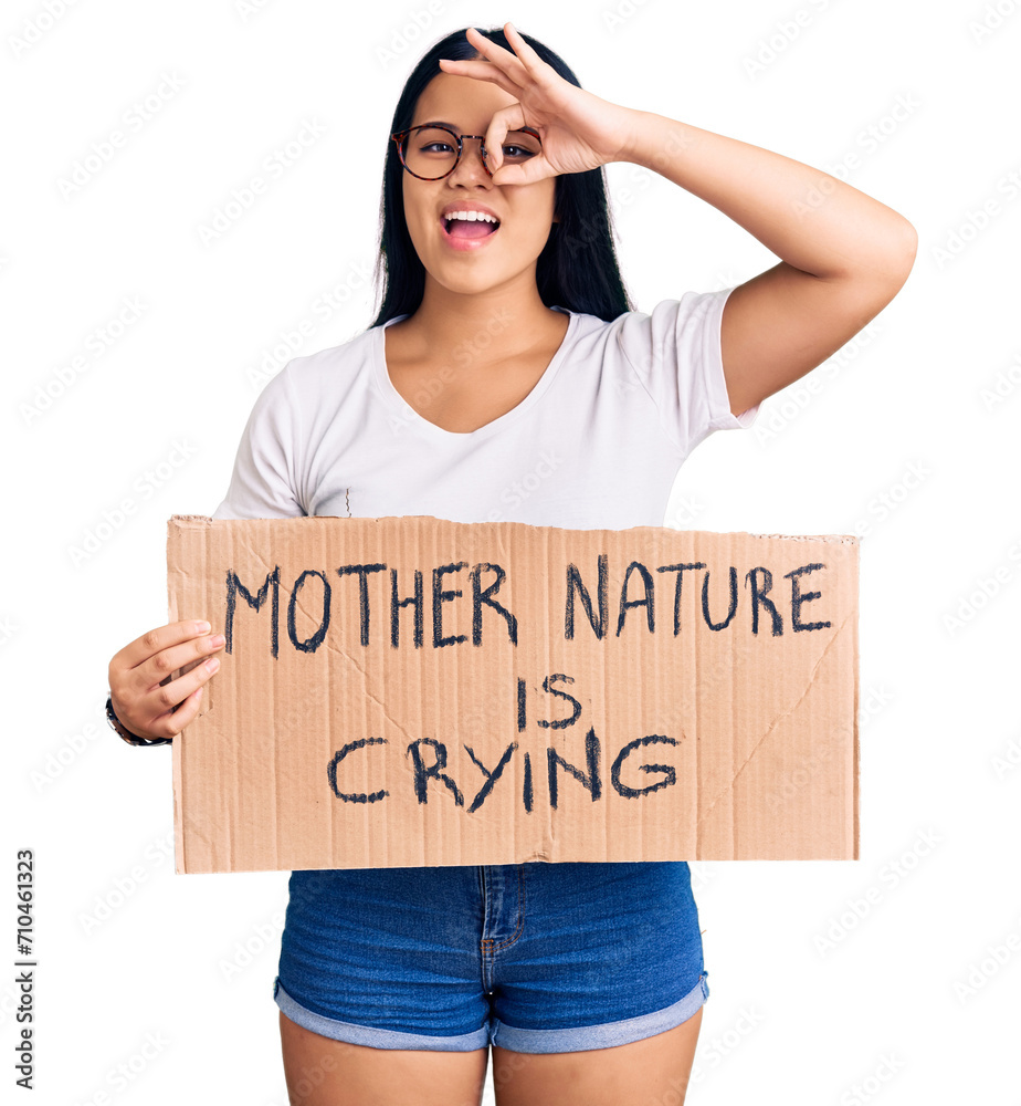 Young beautiful asian girl holding mother nature is crying protest cardboard banner smiling happy doing ok sign with hand on eye looking through fingers Young beautiful asian girl holding mother nature is crying protest cardboard banner smiling happy doing ok sign with hand on eye looking through fingers