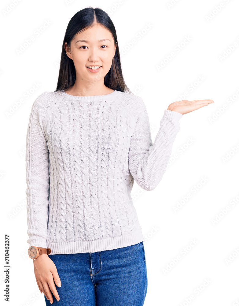 Young beautiful chinese woman wearing casual sweater smiling cheerful presenting and pointing with palm of hand looking at the camera. Young beautiful chinese woman wearing casual sweater smiling cheerful presenting and pointing with palm of hand looking at the camera.