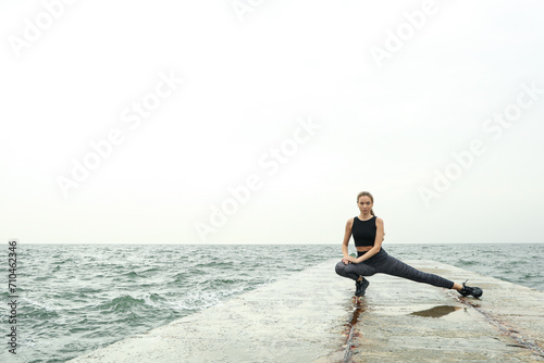 Young woman in sportswear doing yoga on the sea pier, space for text