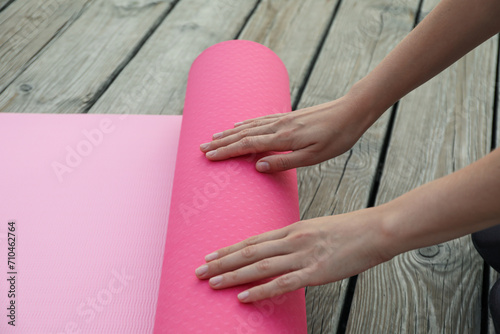 Pink yoga mat and female hands on wooden background, close up