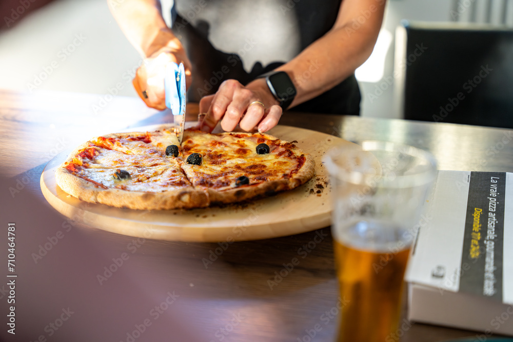 main de femme en train de découper une pizza avec une roulette main de femme en train de découper une pizza avec une roulette