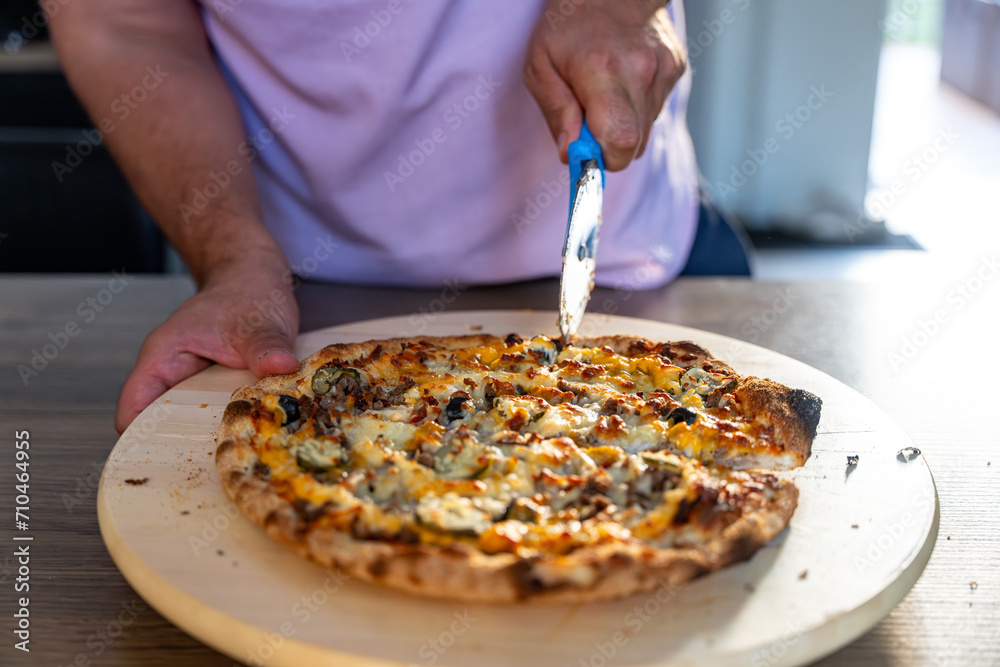 main d'homme en train de découper une pizza avec une roulette