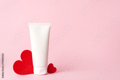 Cosmetic cream white tube with red hearts heart on pink background, copy space photo