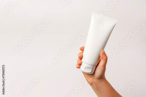 Child little hand holding white cream tube on light background. Daily children beauty product. Closeup. Empty place for text or logo