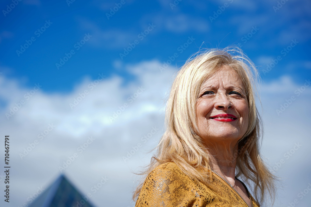 smiling retired woman with blond hair with blue sky in the background smiling retired woman with blond hair with blue sky in the background
