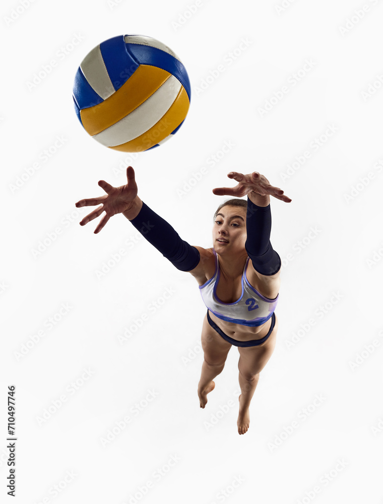 Top view. Dynamic image of athletic female volleyball player in motion, practicing, jumping with ball isolated over white studio background. Concept of professional sport, competition, match, strength