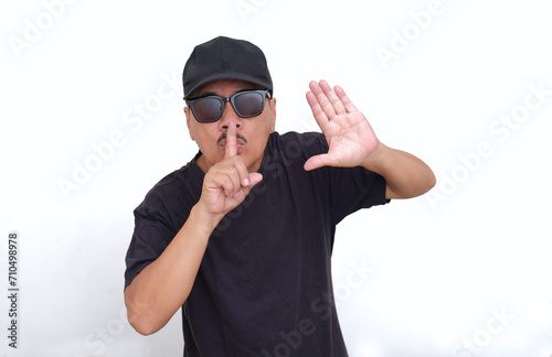 Asian guy in black standing and gesturing to stop making noise with both hands photo