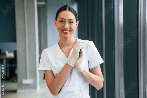 Cheerful female doctor in white coat is indoors standing and smiling