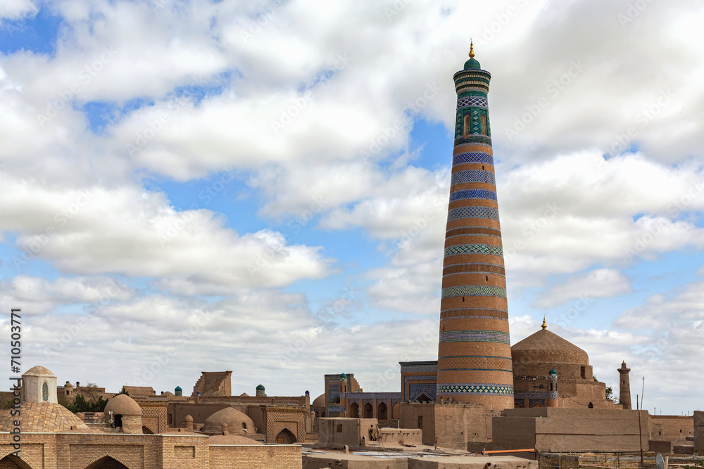 Islam Khoja Minaret in Khiva, Uzbekistan. Best viewpoint at Ichan Kala (ancient city of Khiva). Roof tops. Scenis clouds at background