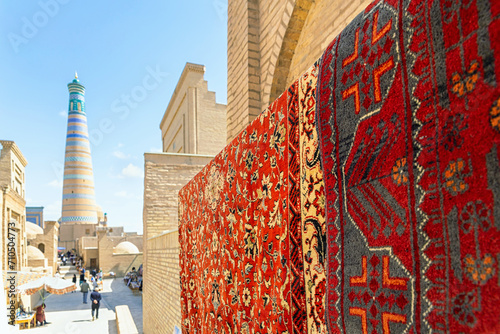 Red color carpets on the street market in front of Islam Khoja Madrasa. Defocused minaret at background. Itchan-Kala, old town of Khiva (Xiva), Uzbekistan photo