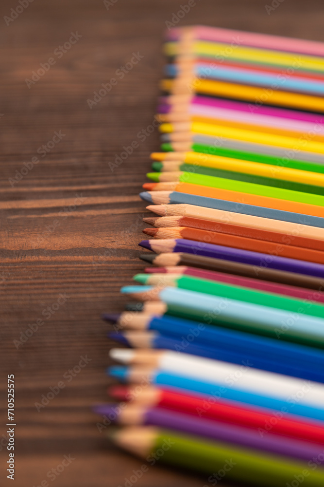 Set of watercolor pencils on brown wooden. Side view, selective focus