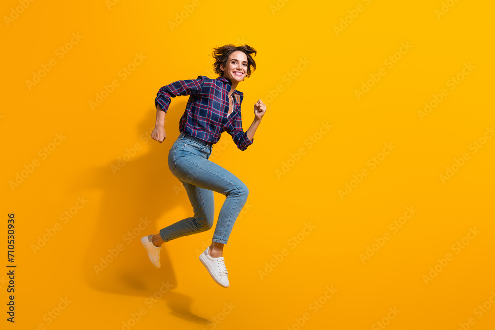 Full size photo of active optimistic nice girl wear checkered blouse hurry running to empty space isolated on yellow color background